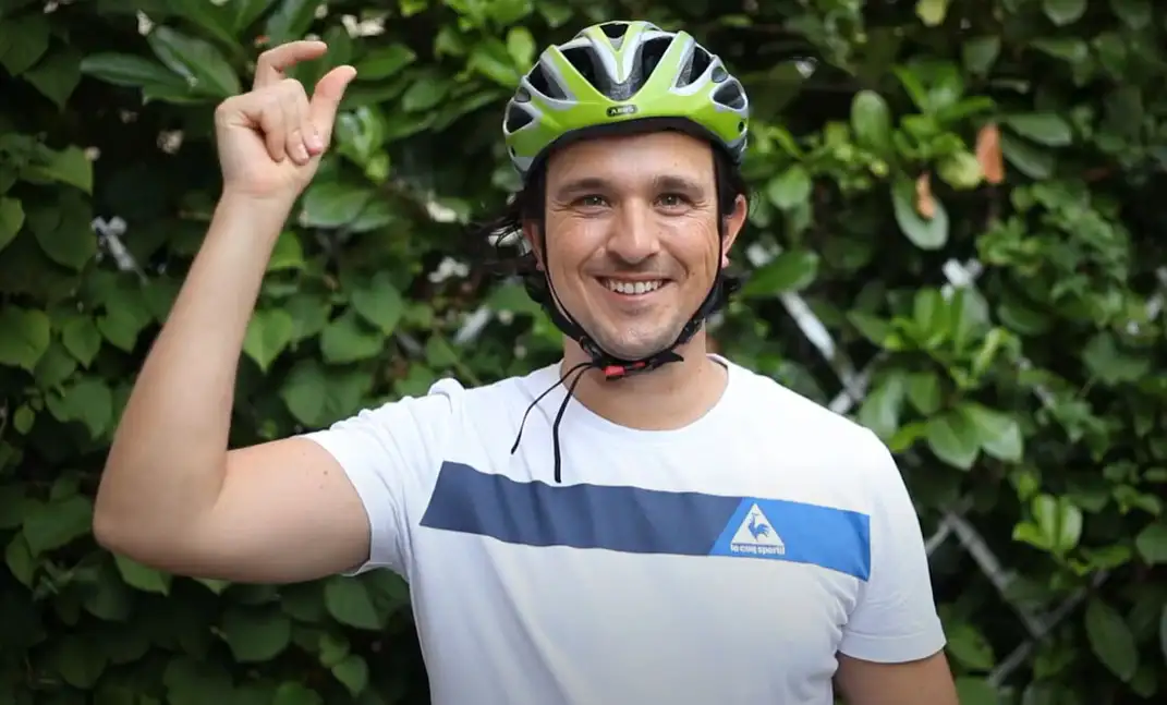 Ein American Express Mitarbeiter mit grünem Fahrradhelm vor einer grünen Hecke